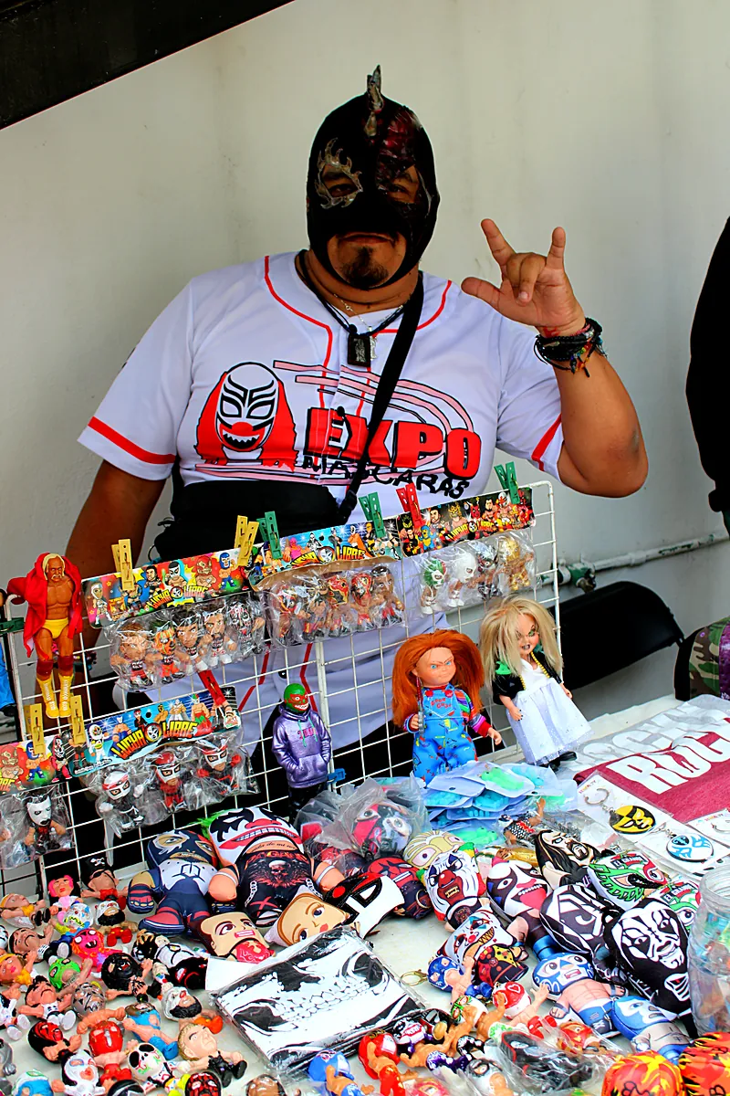Luchador con playera de Expo Máscaras junto a su mercancía original y figuras de lucha libre
