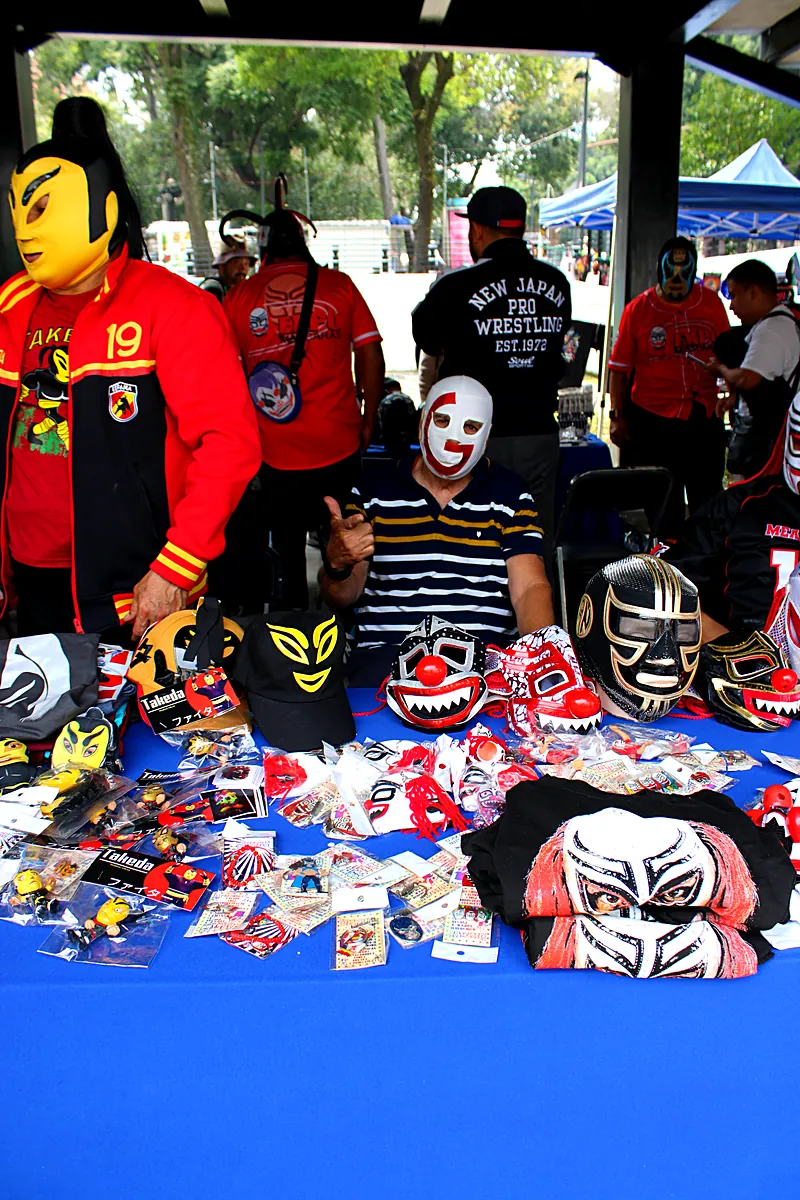 Puesto con máscaras de luchadores originales y luchadores atendiendo al público en Expo Máscaras